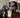 Person pouring a dark liquid into an iced coffee drink on a wooden counter with kitchen utensils in the background.